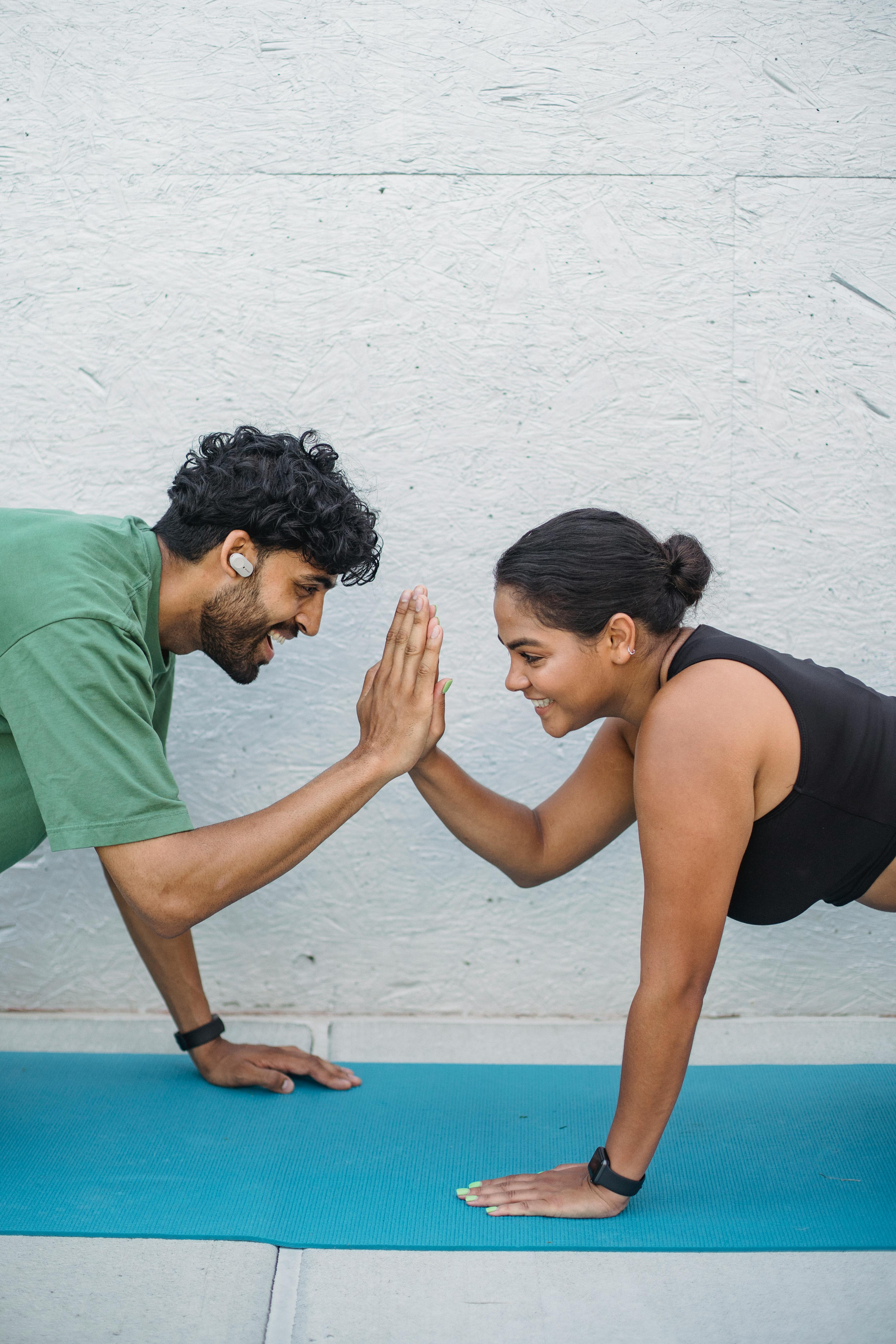 Two people doing partner exercise high-five in plank position on yoga mat